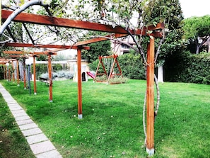 A garden with a wooden pergola, a swing set, and a paved walkway. - Private Room at the Villa nel Verde Residence in Rome-Ciampino (roma)