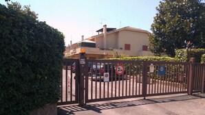 A gated entrance with a speed limit sign, a no parking sign, and a blue sign with a white symbol. - Private Room at the Villa nel Verde Residence in Rome-Ciampino (roma)