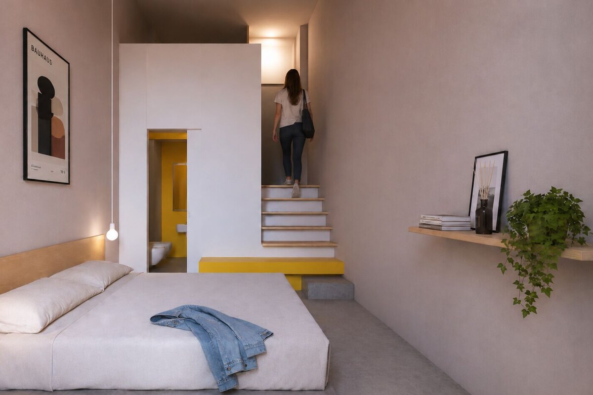 Een slaapkamer met een bed, een bedlampje en een trap naar een badkamer.