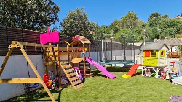Un patio trasero con un parque infantil de madera, un tobogán y un trampolín.