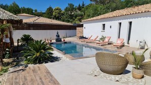 Una piscina con sillas de descanso, una estatua y una cabaña con techo de paja.