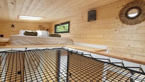 Interior de una cabaña de madera con una cama, una ventana y un espejo montado en la pared.