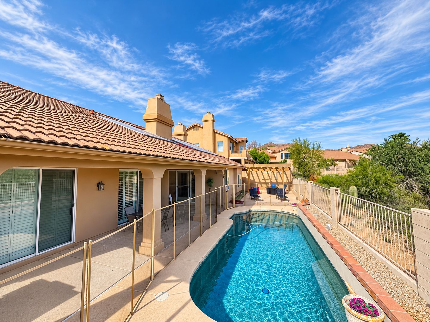 A residential property with a swimming pool, a covered patio, and a view of neighboring houses.