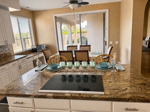A kitchen with a Bosch induction cooktop, white cabinets, a dining area with chairs and a table, and a ceiling fan. - Infrared Sauna, Mountain View’s,Golf,Hiking and infrared red light therapy. (Scottsdale)