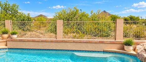 A swimming pool with clear blue water, surrounded by a brick wall and a metal fence.