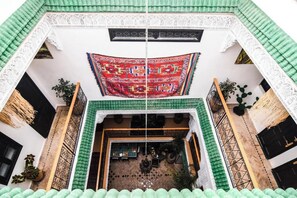 Un patio con un tapete rojo estampado, un tejado de baldosas verdes y una pared blanca con una ventana.