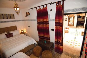 Un dormitorio con cama, mesita de noche, lámpara, una pequeña mesa y vista al patio.