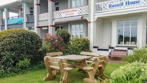 Ein Garten mit einem Holztisch und Bänken, umgeben von verschiedenen Pflanzen und Sträuchern.