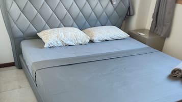A bed with a grey headboard and two pillows, a bedside table with a remote control, and a window with curtains.