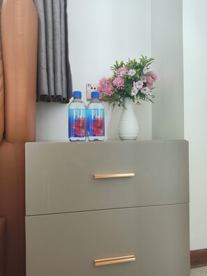 Ein grauer Schrank mit zwei Fiji-Wasserflaschen und einer Vase mit rosa Blumen.