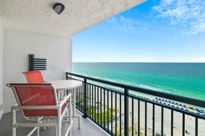 A balcony with a white table and red chairs, overlooking a beach with umbrellas and people. - 🌴Gulf Front~Pools~Onsite Restaurant~Balcony~Sauna~1BR SunDestin 1405🌴 (Destin)