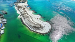 Eine Luftaufnahme einer Küstenlandschaft mit einer Marina, einem Sandstrand und klarem, blauem Wasser.