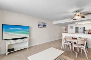A living room with a flat-screen TV, a dining area with a table and chairs, a kitchen with a refrigerator, and a ceiling fan. - 🌴Gulf Front~Pools~Onsite Restaurant~Balcony~Sauna~1BR SunDestin 1405🌴 (Destin)