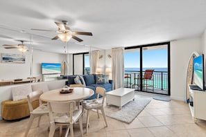 A modern living room with a large sofa, a dining table, and chairs. There is a balcony with a view of the ocean. - 🌴Gulf Front~Pools~Onsite Restaurant~Balcony~Sauna~1BR SunDestin 1405🌴 (Destin)
