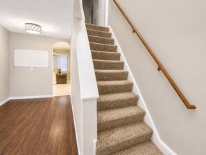 A staircase with carpeted steps and a wooden handrail, leading to a landing with a whiteboard and a window. - Modern Tulsa Haven  Near Jenks (Tulsa)
