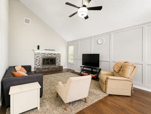A living room with a fireplace, a sofa, a recliner, a TV stand, and a ceiling fan.