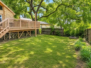 A backyard with a wooden deck, a stone wall, and a fire pit. - Modern Tulsa Haven  Near Jenks (Tulsa)