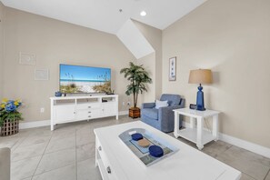 A living room with a flat-screen TV, a sofa, a coffee table, a lamp, and a plant. - 🌴 Sunny Beach Days | 🏖️ Walk to Beach | 🌊 Gulf Views (Panama City Beach)