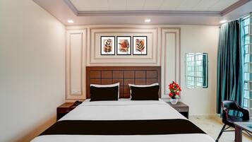 A hotel room with a large bed, a nightstand, a chair, a window with curtains, and artwork on the wall.