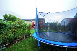 A trampoline in a backyard with a safety net, surrounded by greenery and a wooden fence.