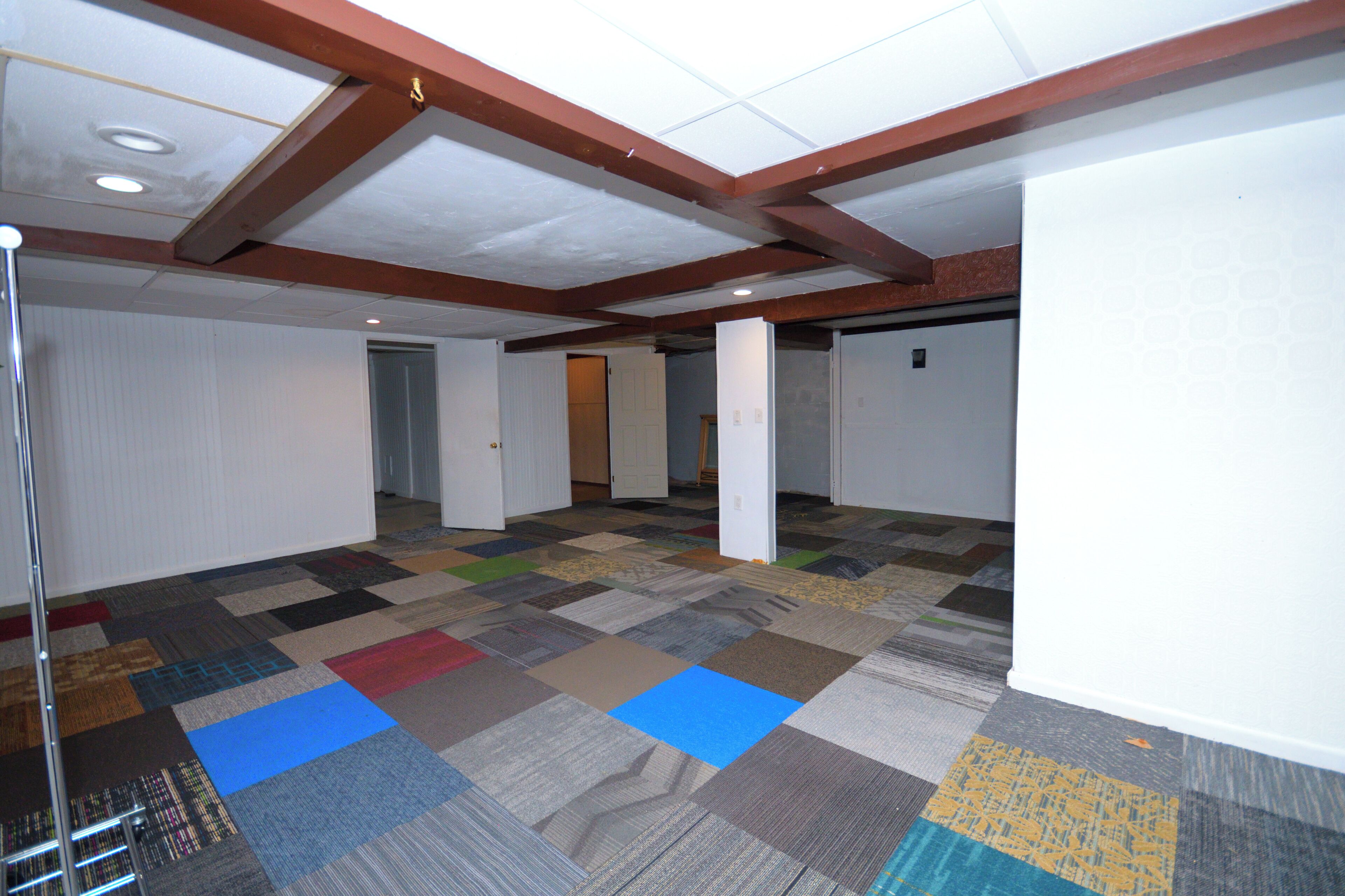 Une pièce spacieuse avec un tapis à motifs, des poutres en bois au plafond et des murs blancs.