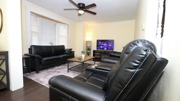 A living room with a black leather sofa, a coffee table, a television, and a ceiling fan.