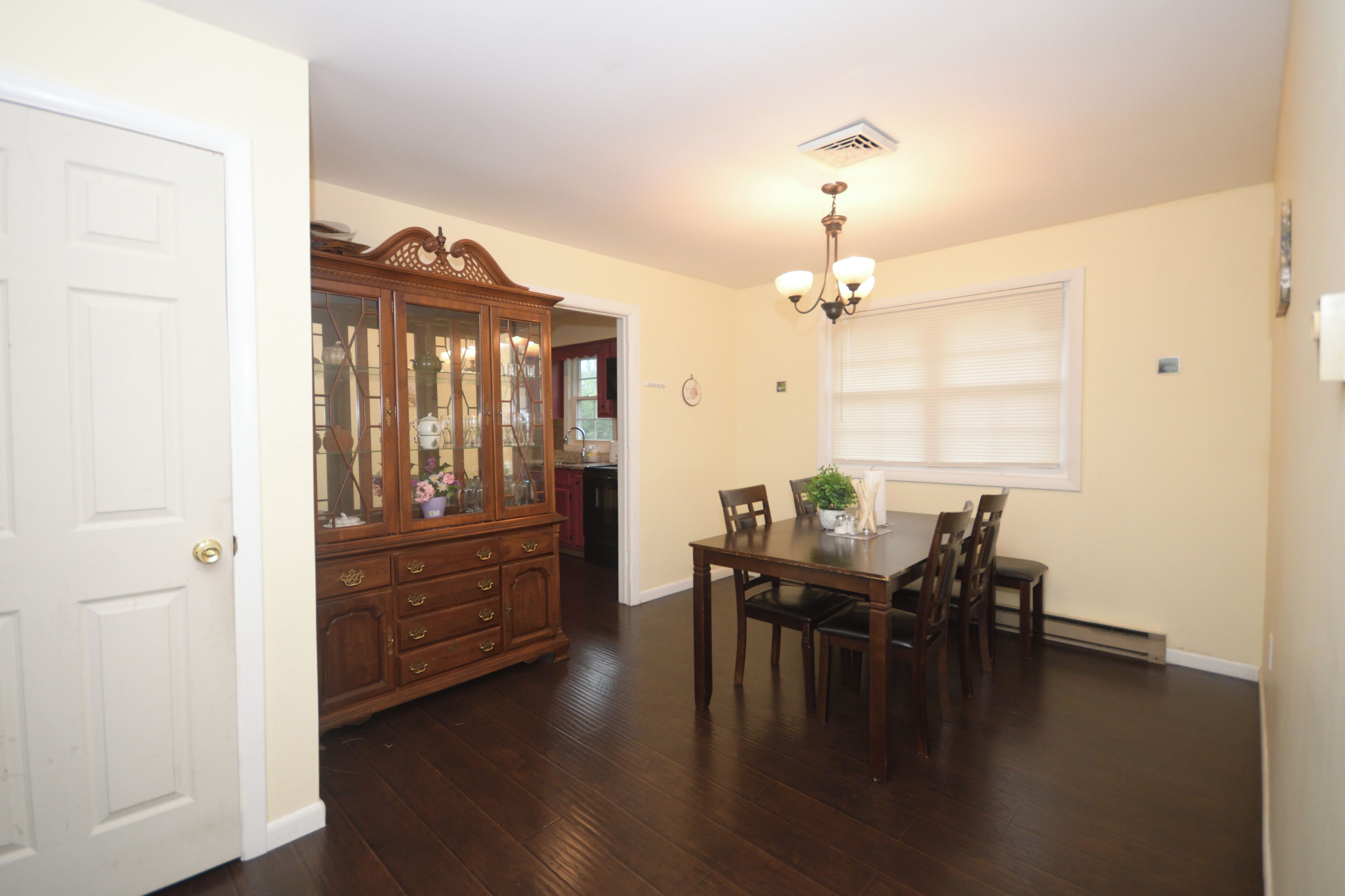 A dining area with a wooden table and chairs, a cabinet with glass doors, and a ceiling light fixture.