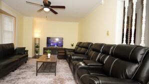 A living room with a sofa, a coffee table, a television, and a ceiling fan.
