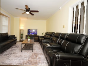 A living room with a sofa, a coffee table, a television, and a ceiling fan.
