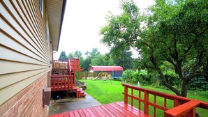 A wooden deck with a red railing, a brick wall, and a grassy yard with a swing set.