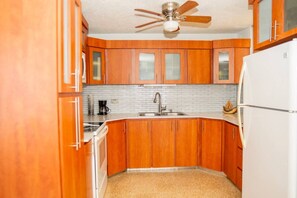 Eine kleine Küche mit Holzausstattung, einem weißen Kühlschrank, einer Kaffeemaschine und einem Deckenventilator.