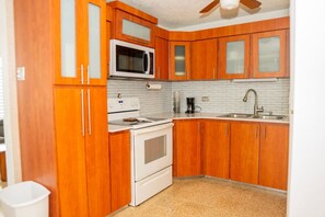A kitchen with wooden cabinets, a microwave, a stove, and a sink. - Casa Julia Tropical Beach Stay (Luquillo)