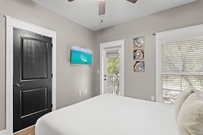 A bedroom with a large bed, a black door, a television on the wall, and a window with blinds. - 🚲Willow & Waves | Golf Cart, 4 Bikes, Pool, Near Beach🏊 (Inlet Beach)