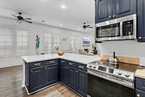A modern kitchen with dark cabinetry, a central island, stainless steel appliances, and a ceiling fan. - 🚲Willow & Waves | Golf Cart, 4 Bikes, Pool, Near Beach🏊 (Inlet Beach)