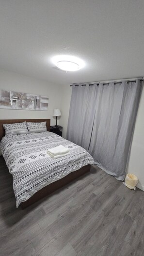 A neatly made bed with patterned bedding, a bedside lamp, and a grey curtain.