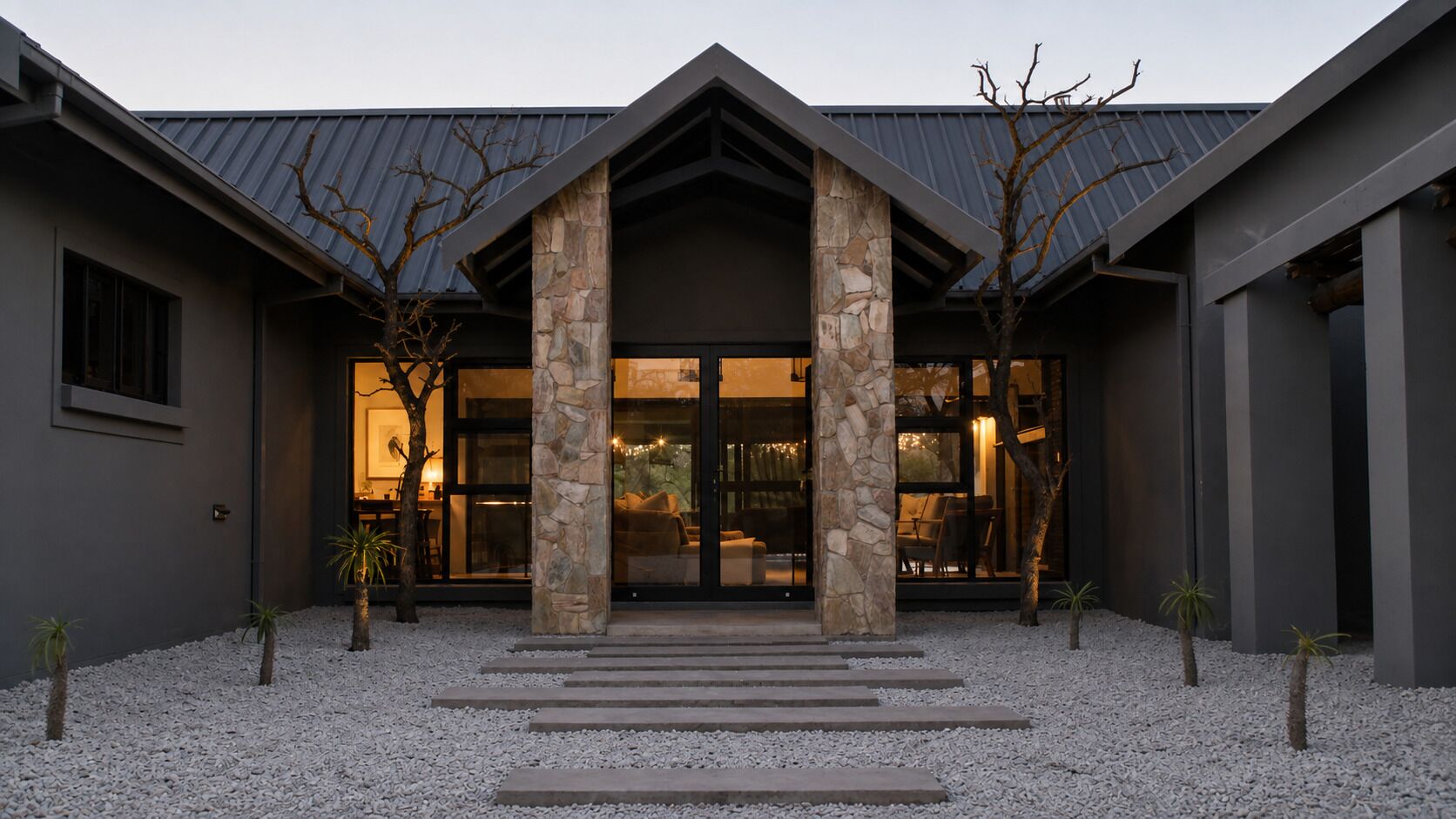 A modern building with a stone facade, large glass windows, and a gravel driveway.