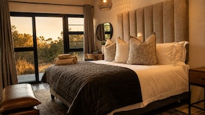A bedroom with a large bed, a bench, a bedside table, and a view through a window. - Villa Thula (Hoedspruit)