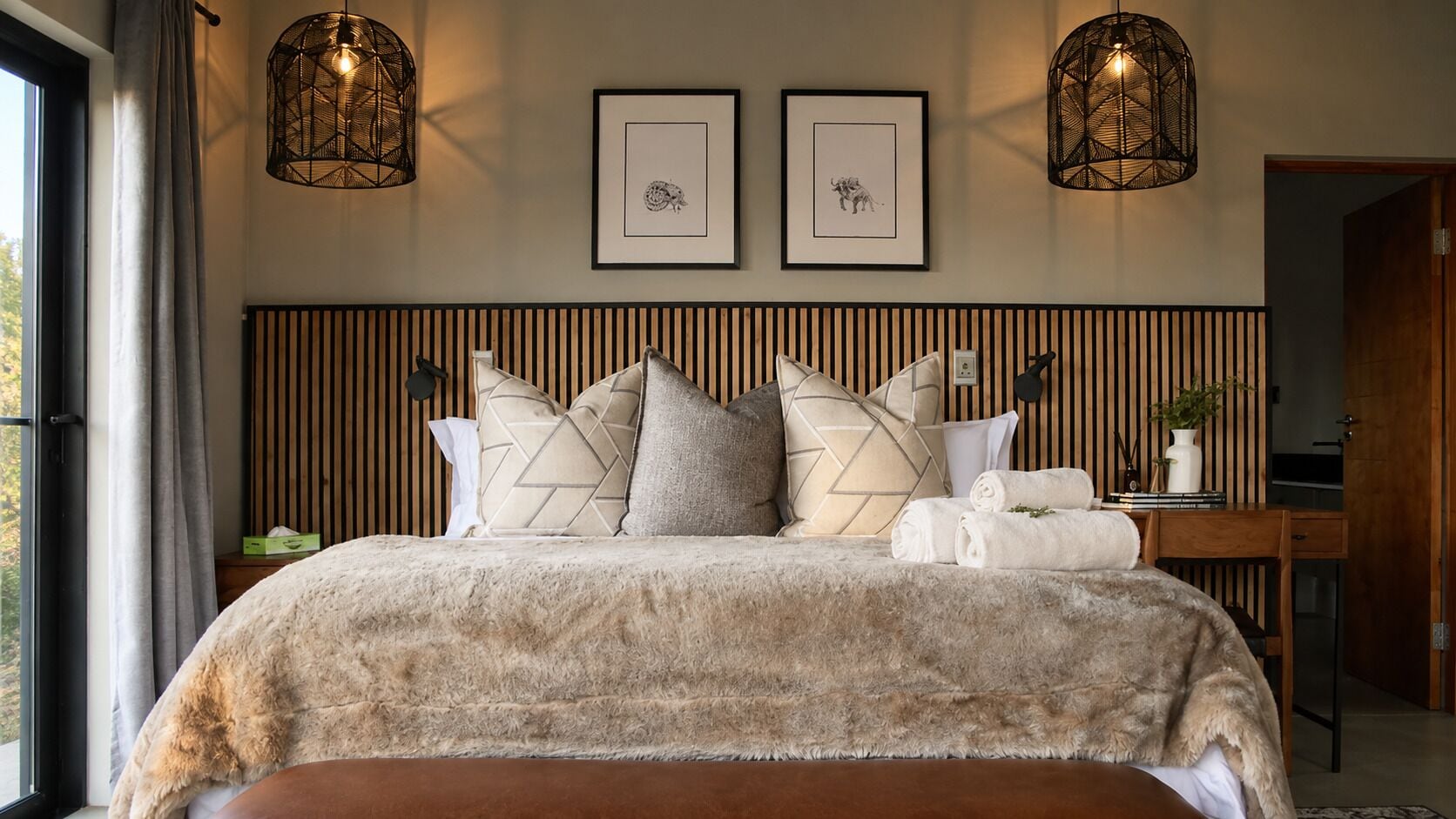 Une chambre à coucher avec un lit, des oreillers, une table de chevet, une lampe et des tableaux encadrés accrochés au mur.