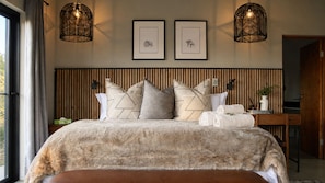 Un dormitorio con cama, almohadas, una mesita de noche, una lámpara y cuadros en la pared.