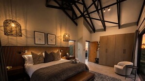A bedroom with a large bed, a bench, a wardrobe, and a view of the outdoors.