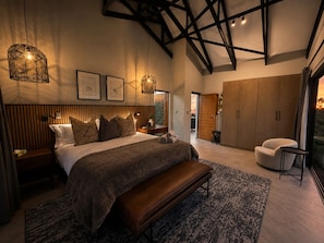 A bedroom with a large bed, a bench, a wardrobe, and a view of the outdoors. - Villa Thula (Hoedspruit)