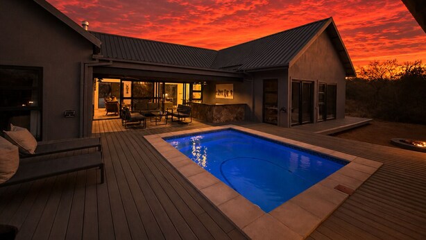 A modern house with a swimming pool, outdoor seating, and a sunset sky.