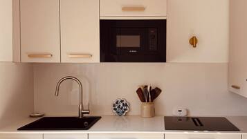 A modern kitchen with white cabinetry, a Bosch microwave, a sink, and a countertop with a utensil holder.