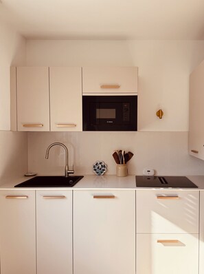 A modern kitchen with white cabinetry, a Bosch microwave, a sink, and a countertop with a utensil holder. - SARLAT ON FOOT - PARKING SPACE - ELEVATOR - 160X200 BED - WIFI & NETFLIX (Sarlat-la-Canéda)
