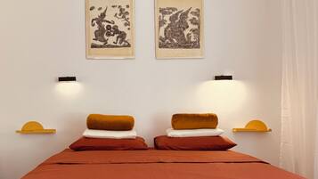 A room with a bed, two wall-mounted lamps, and two framed artworks.