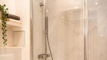 A modern bathroom with a glass-enclosed shower, a white toilet, and a small shelf with towels and a plant.
