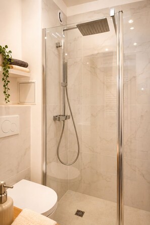 A modern bathroom with a glass-enclosed shower, a white toilet, and a small shelf with towels and a plant. - SARLAT ON FOOT - PARKING SPACE - ELEVATOR - 160X200 BED - WIFI & NETFLIX (Sarlat-la-Canéda)