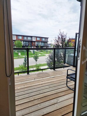 Eine Holzterrasse mit schwarzer Geländer, mit Blick auf eine Straße mit Gebäuden und blauem Himmel.