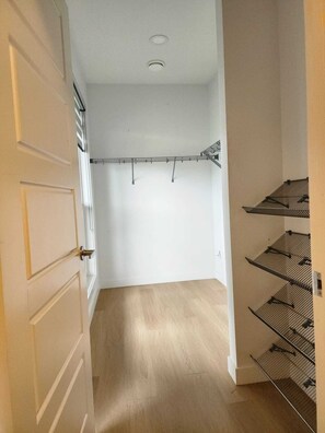A narrow hallway with a wooden floor leading to a closet with metal shelving. - The Edmonton Nest (Edmonton)