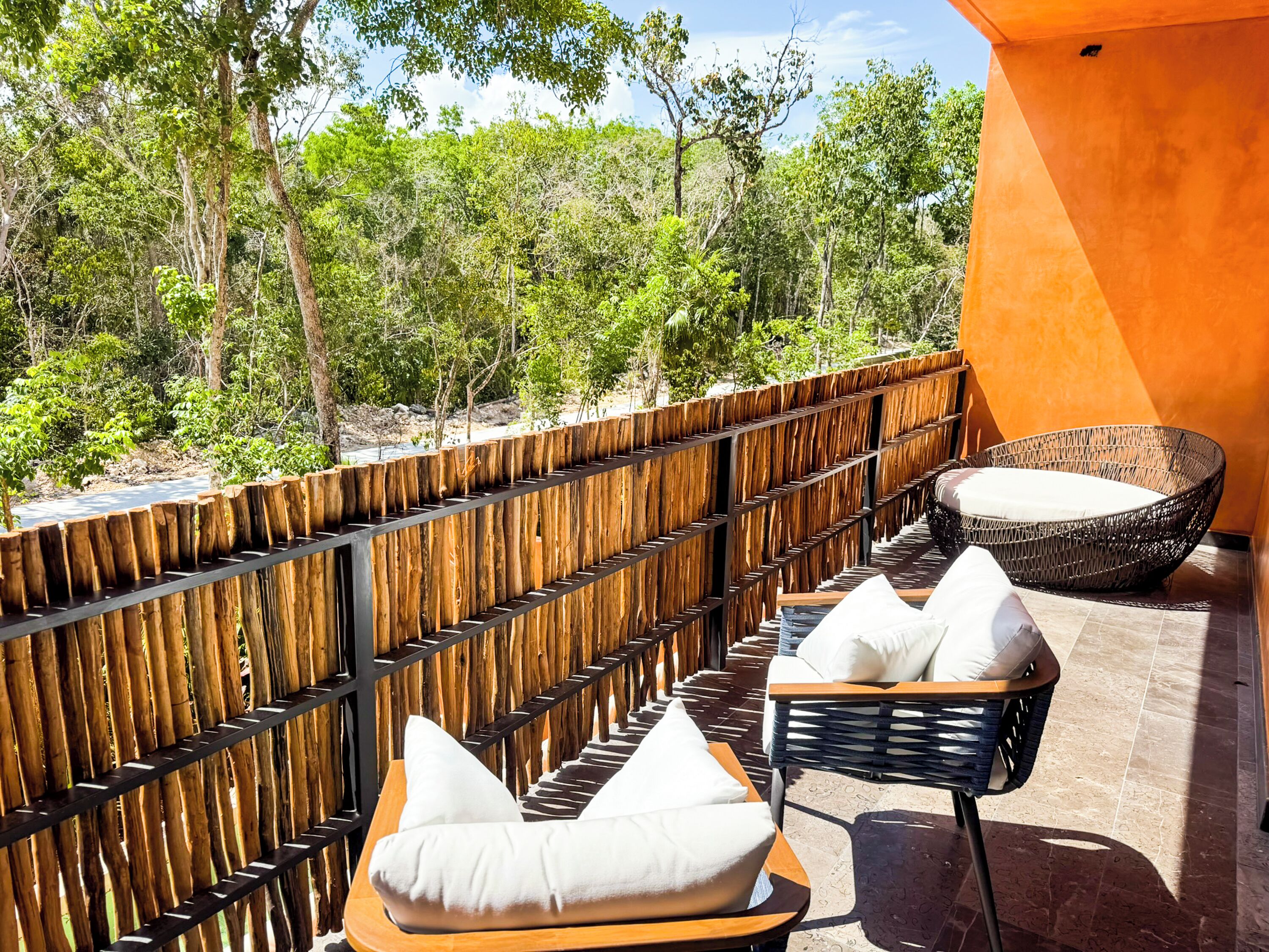 A balcony with a wooden fence, wicker furniture, and a view of a forested area.
